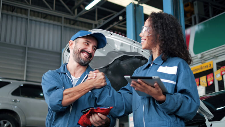 An auto mechanic school grad shaking hands with a colleague in a garage