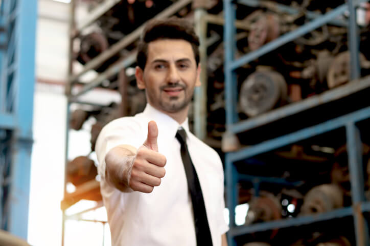 A friendly male auto parts manager giving the thumbs-up sign in a store after completing his auto parts training