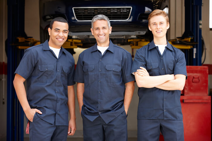 A trio of smiling auto mechanics taking a group photo at our automotive school