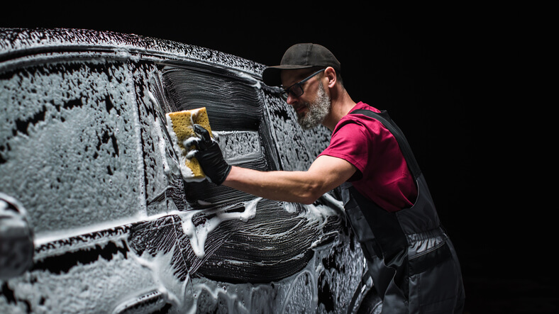 A male auto detailing professional washing the exterior of an electric vehicle after completing his auto detailing training