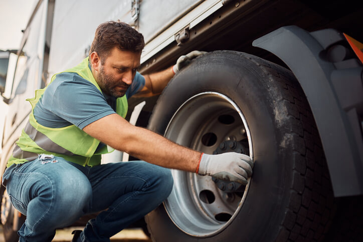 A male dispatcher examining a truck's tires for safety after completing his dispatch training