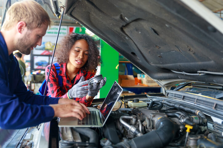 A male auto mechanic instructing a female auto mechanic trainee