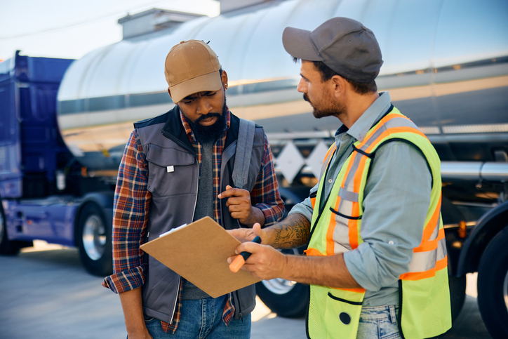 A truck dispatcher and driver reviewing a shipment list together in a parking lot, showcasing the collaborative nature of logistics in auto careers.