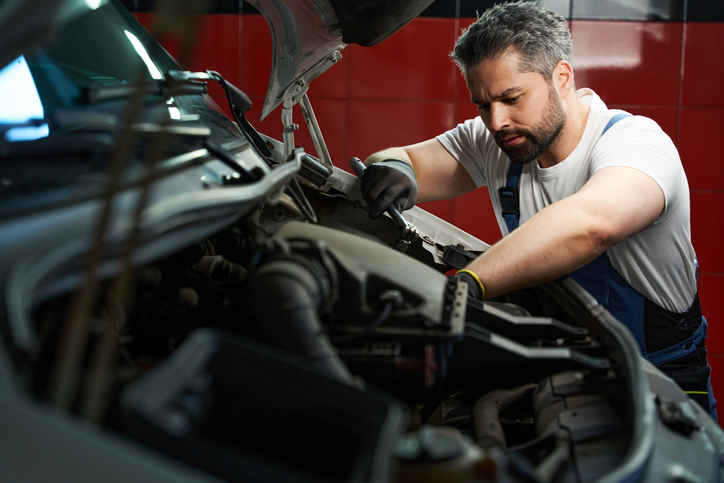 Focused male auto mechanic working on the engine of a vehicle after completing auto mechanic training