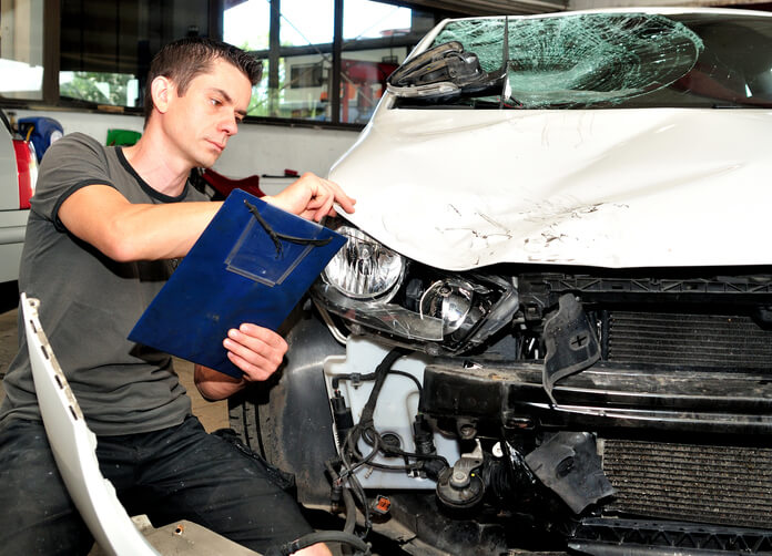 A male auto body estimating professional inspecting a damaged vehicle at a repair shop after completing his automotive training