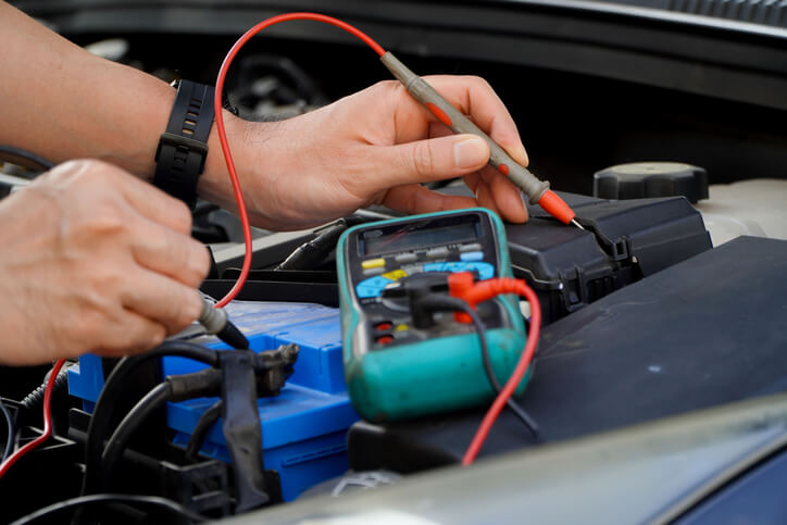 An auto repair technician measuring the voltage of an EV battery with a multimeter after completing his hybrid and electrical mechanic training