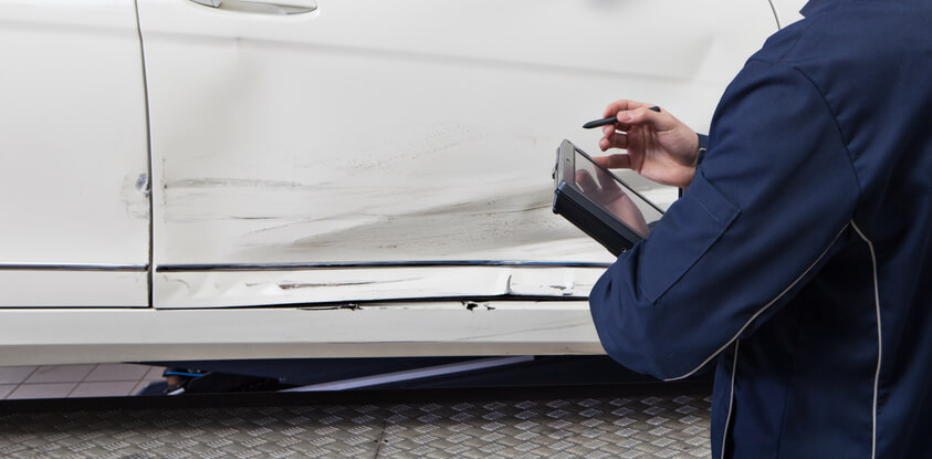 A technician assessing structural damage on a vehicle’s frame after completing his auto body training.