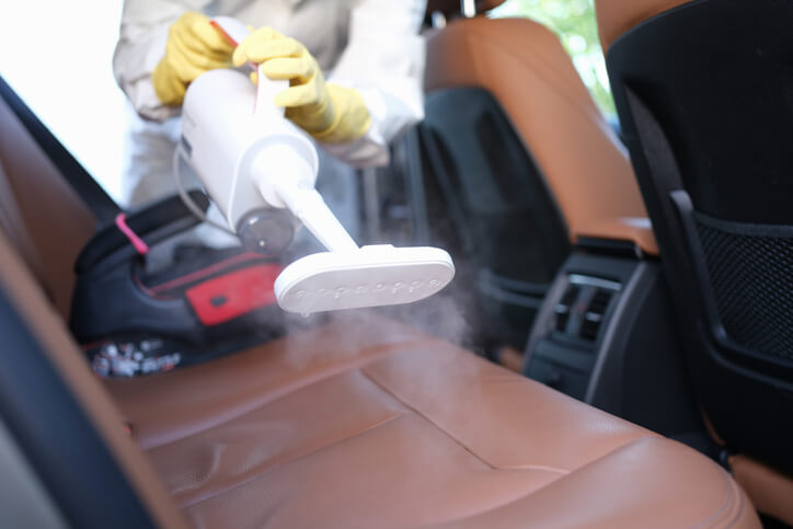 An auto detailing training grad steam cleaning a brown leather car interior