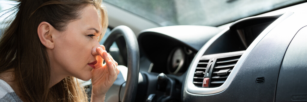 An auto detailing training grad plugging her nose in a smelly car