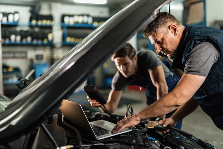 An auto mechanic student learning to operate an electronic vehicle scanning tool in an auto mechanic school.