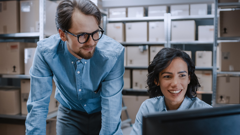 A manager coaching a female trainee through shipment tracking after her dispatch training.