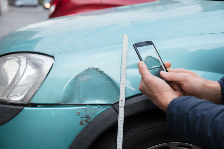 An auto body estimator taking a picture of a dent in a vehicle’s panel after completing his auto body training.