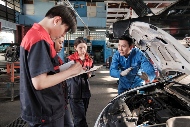 A group of students in auto tech training listening to an in-shop lesson from an instructor