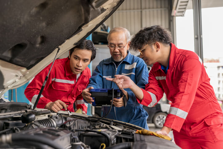 Auto mechanic students being taught by an experienced mechanic in an auto mechanic school