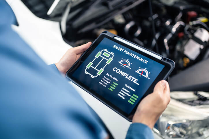 A maintenance technician using a diagnostic tablet to troubleshoot vehicle systems in an automotive school.