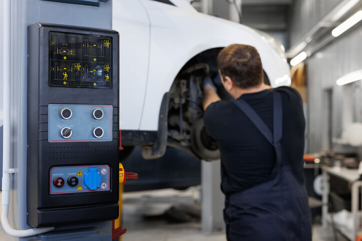 A mechanic operating a modern vehicle lift in an auto repair shop after completing his auto mechanic training