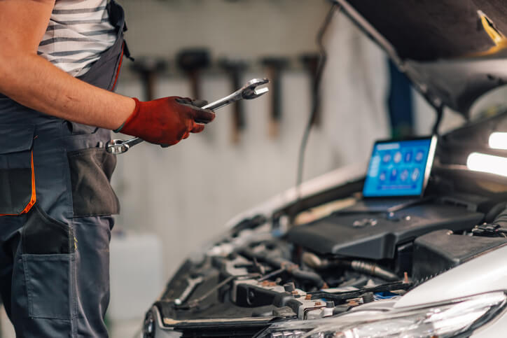 An auto body estimating training grad inspecting a car while holding a tablet