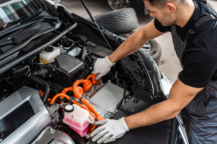 A mechanic inspecting a hybrid car’s engine at a workshop after hybrid and electrical mechanic training