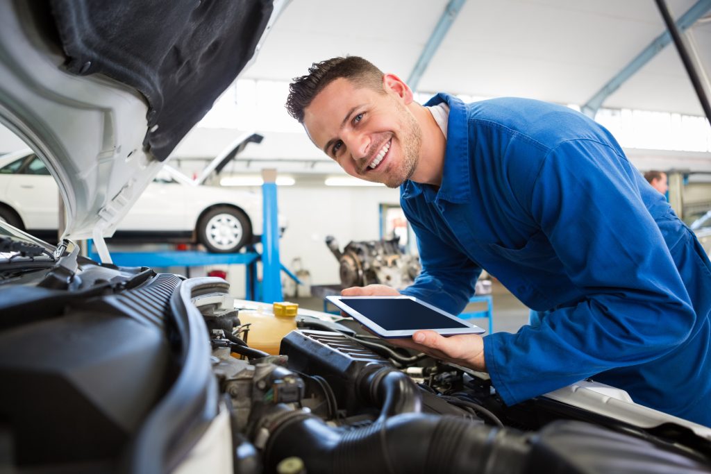 An auto mechanic working under the hood of a car in a repair shop after completing auto mechanic training