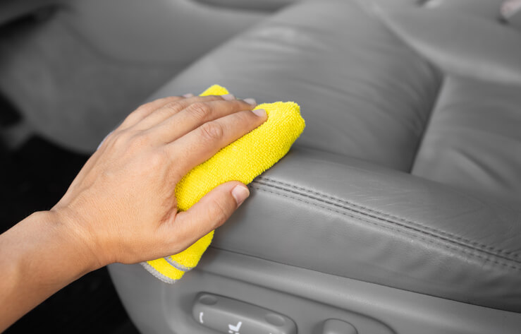 An auto detailing professional applying leather conditioner to a car seat.